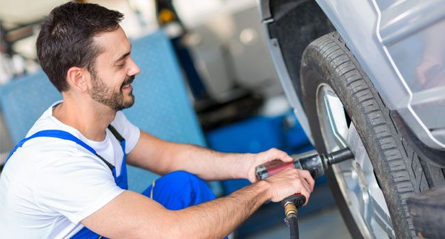 Male mechanic using impact wrench to remove the wheel from a car